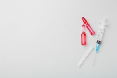 Photo of Glass ampoules with liquid and syringe on white background, flat lay. Space for text