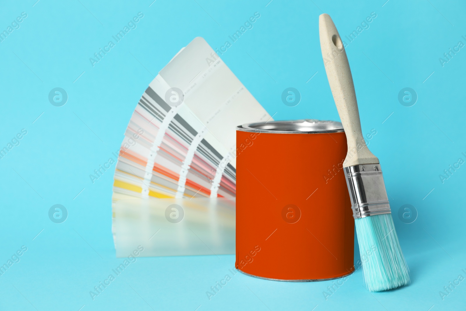 Photo of Can of orange paint, color palette samples and brush on turquoise background