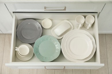 Clean plates, cups, butter dish and bowl in drawer indoors, top view