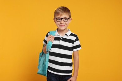 Happy schoolboy in glasses with backpack on orange background