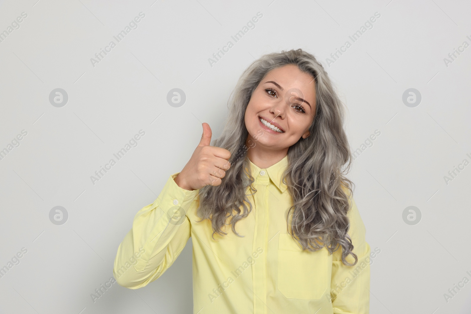 Image of Portrait of smiling woman with ash hair color showing thumb up gesture on light background