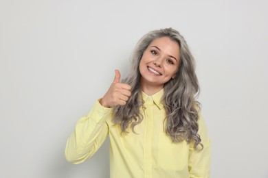 Image of Portrait of smiling woman with ash hair color showing thumb up gesture on light background