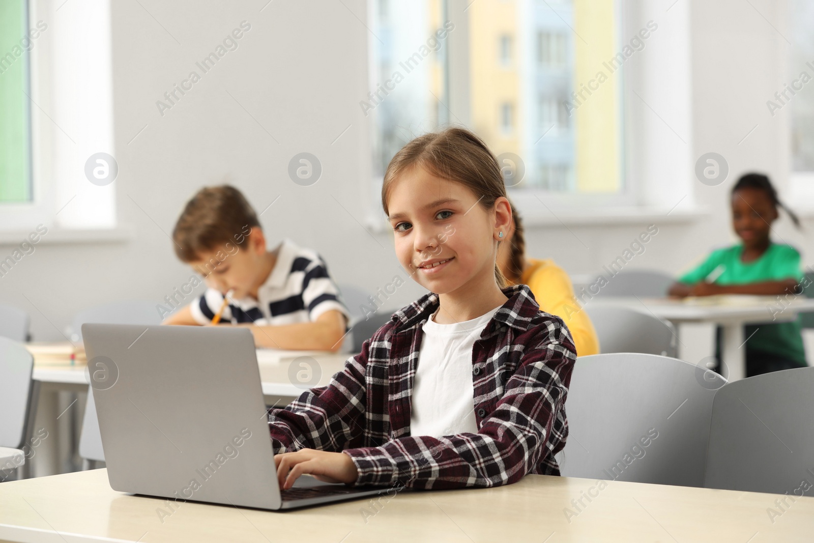 Photo of Smiling little girl with laptop studying in classroom at school