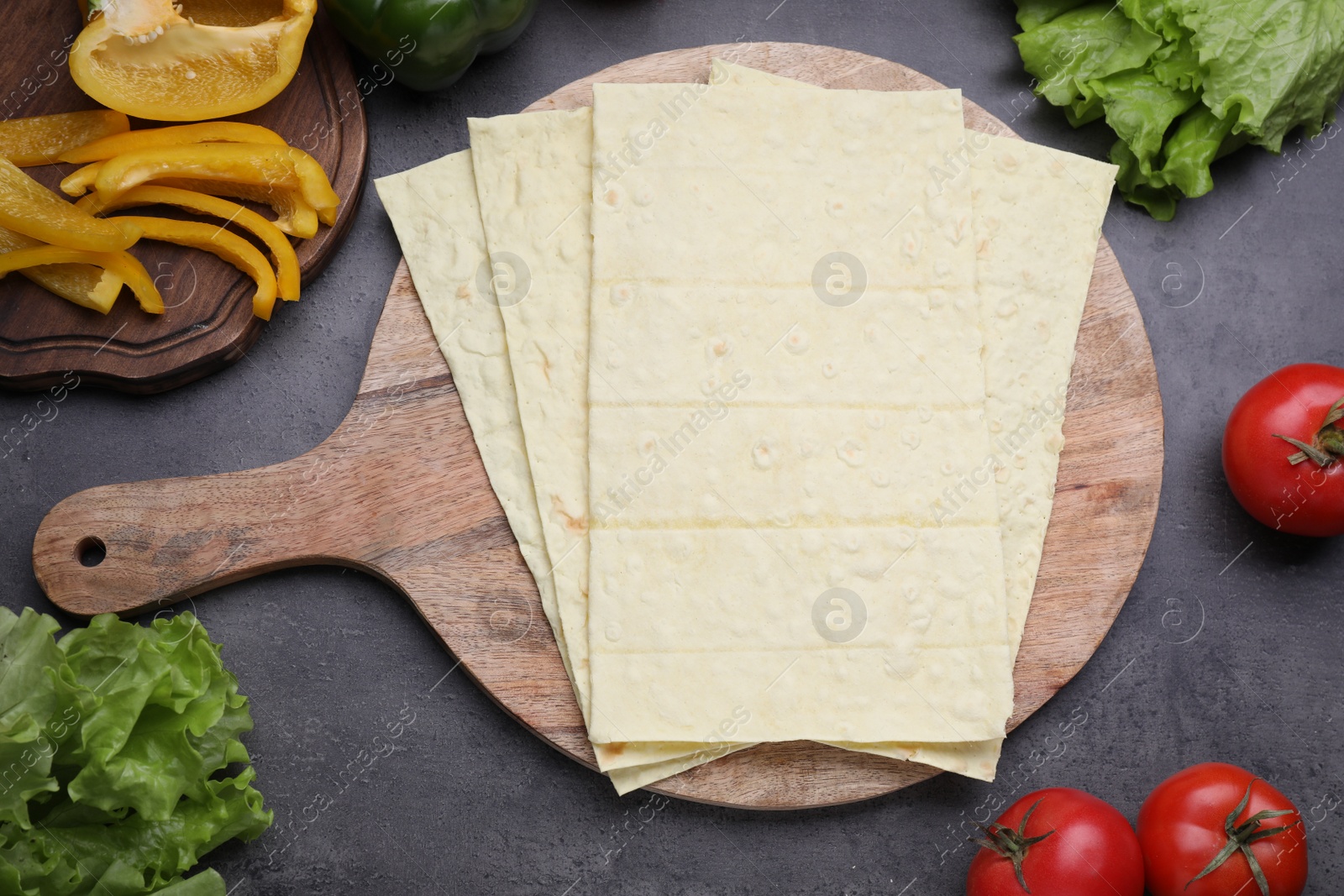 Photo of Delicious Armenian lavash and fresh vegetables on dark table, flat lay