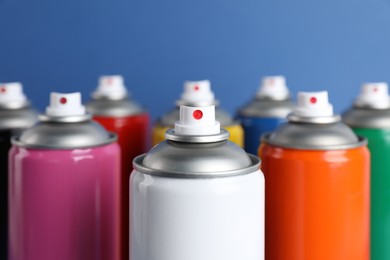 Photo of Colorful cans of spray paints on blue background, closeup