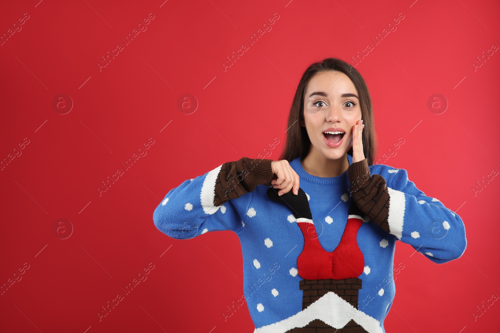 Photo of Surprised young woman in Christmas sweater on red background, space for text