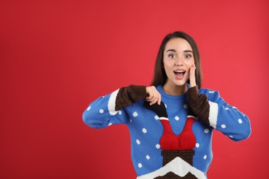 Photo of Surprised young woman in Christmas sweater on red background, space for text