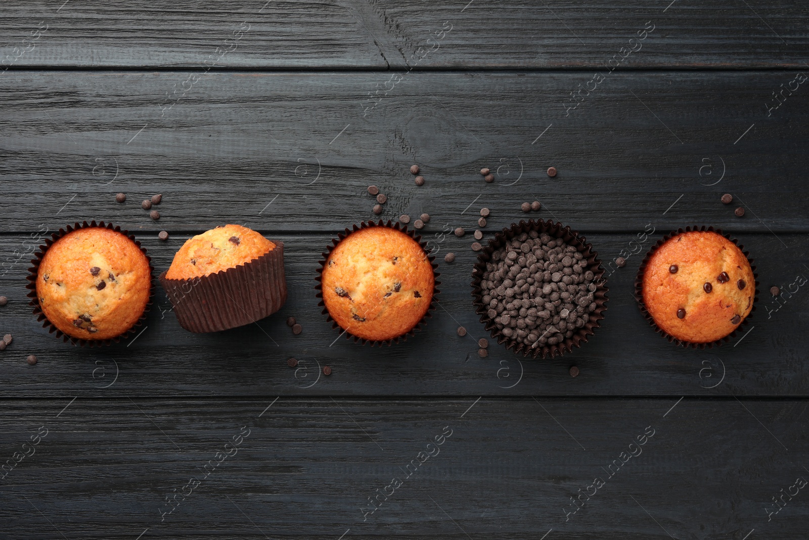 Photo of Delicious freshly baked muffins with chocolate chips on dark gray table, flat lay