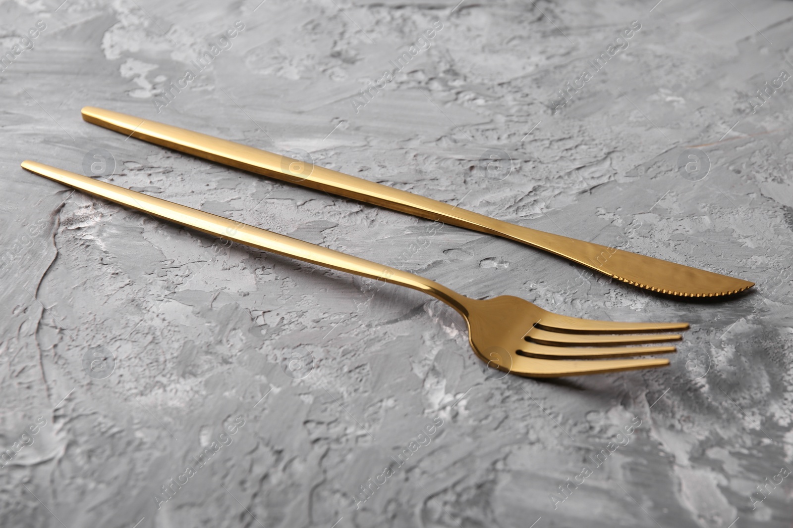 Photo of Stylish cutlery. Golden knife and fork on grey textured table
