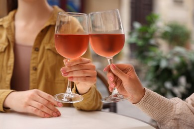 Women clinking glasses with rose wine at white table in outdoor cafe, closeup
