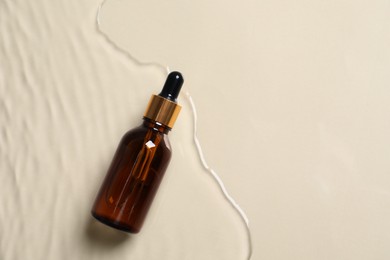 Photo of Bottle of cosmetic oil in water on beige background, top view. Space for text