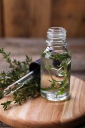 Photo of Bottle of thyme essential oil and fresh plant on wooden board, closeup