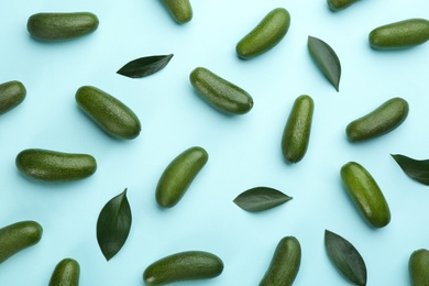Photo of Whole seedless avocados with green leaves on light blue background, flat lay