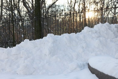 Photo of Pile of snow, fence and sunbeams shining through trees in winter park