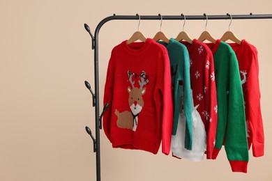 Photo of Rack with different Christmas sweaters on beige background, space for text