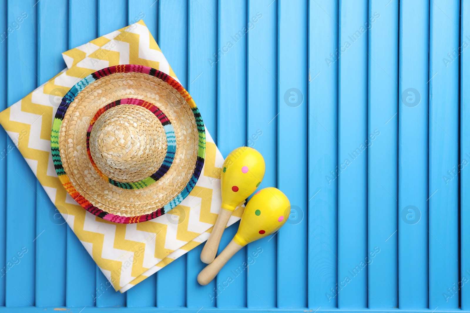 Photo of Mexican sombrero hat, towel and maracas on blue wooden surface, top view. Space for text