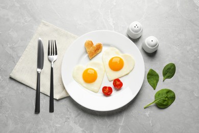Photo of Heart shaped fried eggs with toast served on marble table, flat lay