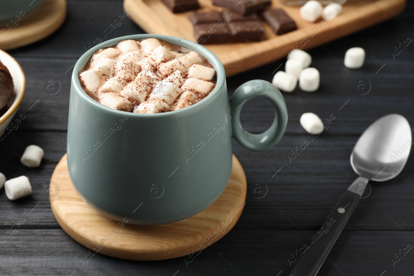 Photo of Cup of aromatic hot chocolate with marshmallows and cocoa powder served on dark gray wooden table, closeup