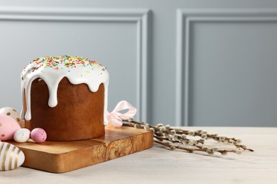 Photo of Delicious Easter cake with sprinkles, decorated eggs and willow branches on white wooden table near light grey wall indoors. Space for text