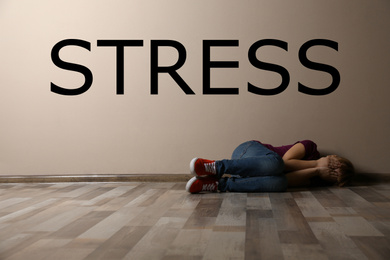 Word STRESS and depressed young woman lying on floor indoors 