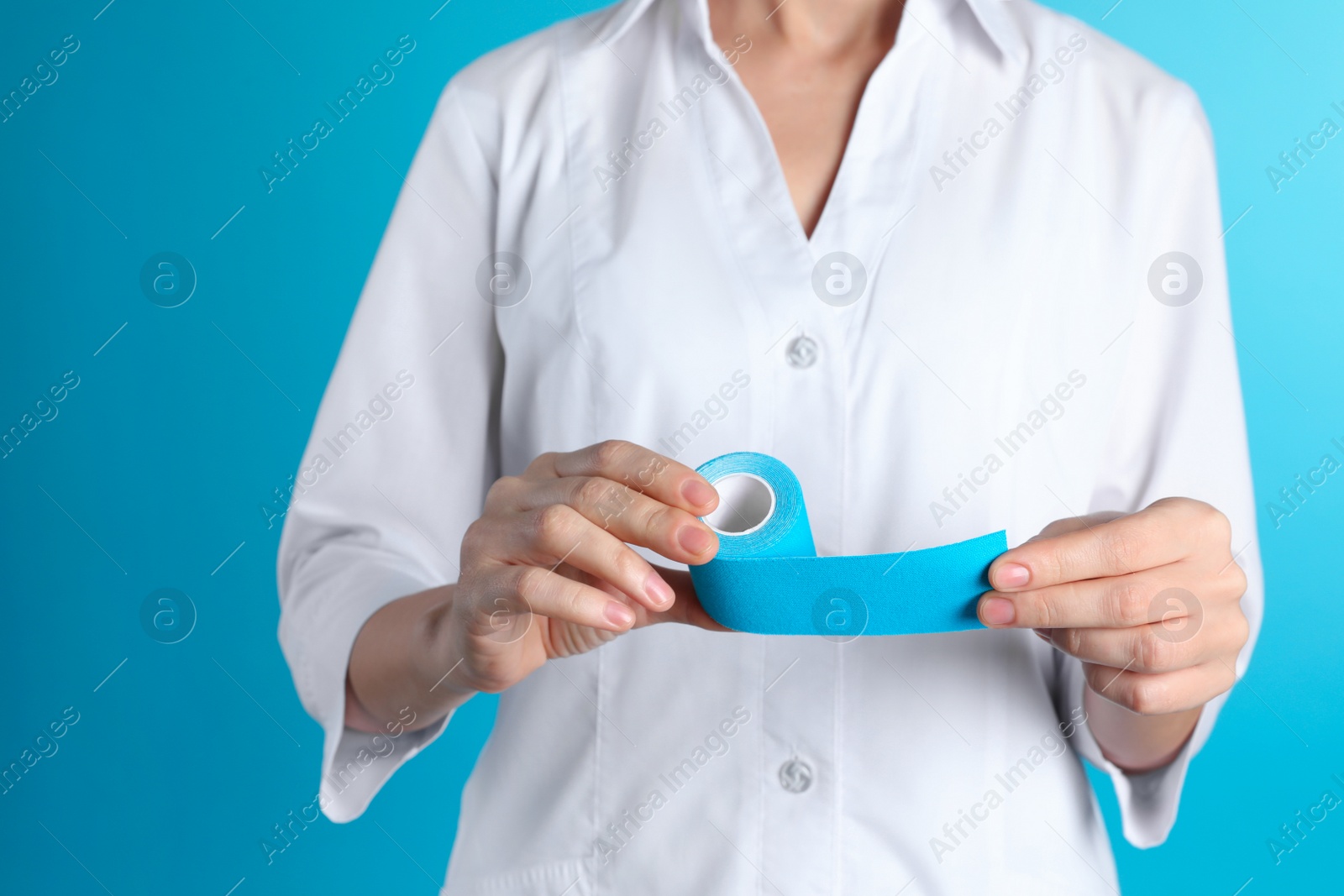 Photo of Female doctor holding elastic therapeutic tape on color background, closeup. Medical object