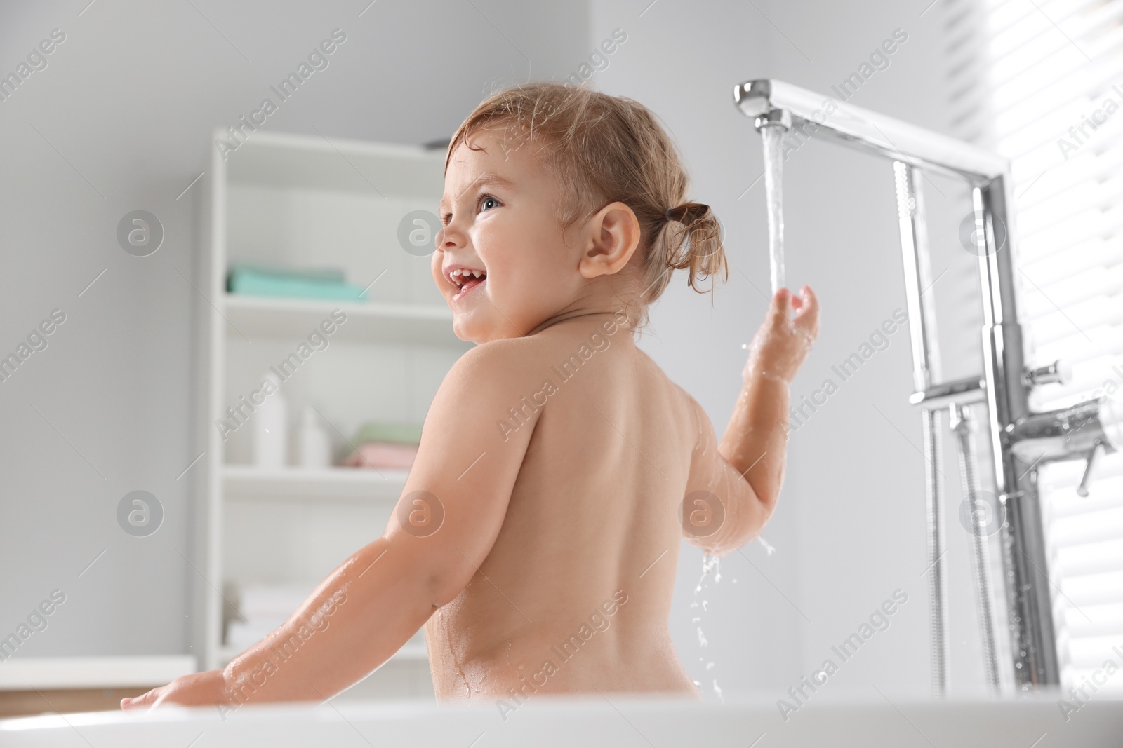 Photo of Cute little girl playing with faucet in bathtub at home