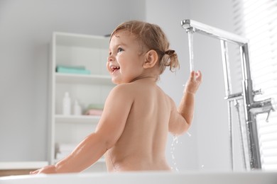 Photo of Cute little girl playing with faucet in bathtub at home