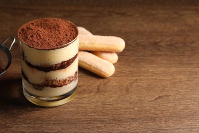 Delicious tiramisu in glass and biscuits on wooden table. Space for text