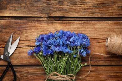 Photo of Bouquet of beautiful cornflowers with scissors and twine on wooden table, flat lay