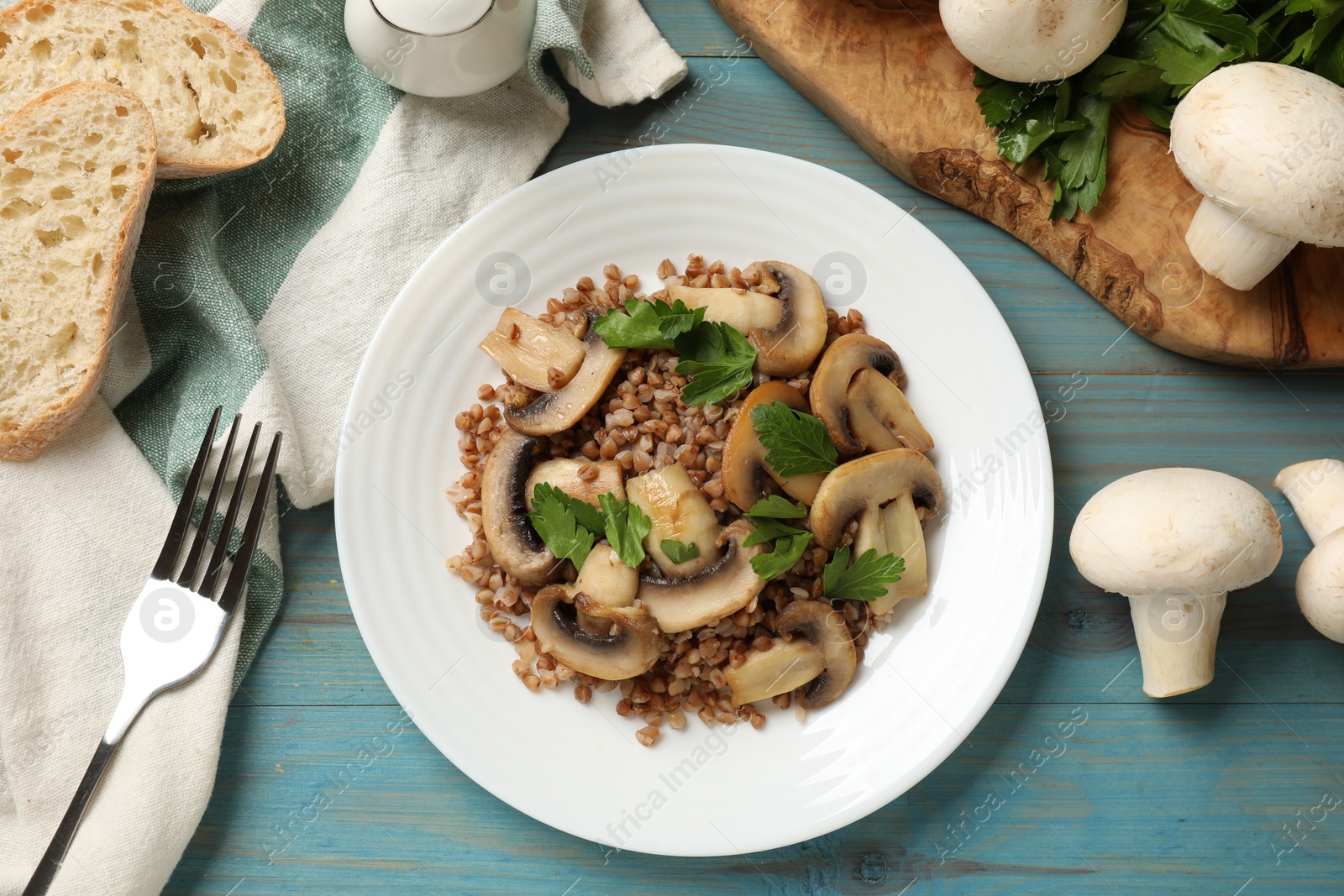 Photo of Tasty buckwheat with fresh parsley and mushrooms on light blue wooden table, flat lay