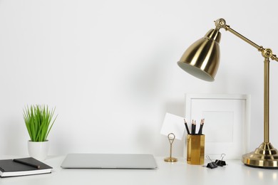 Photo of Cozy workspace with laptop, lamp and stationery on white desk at home