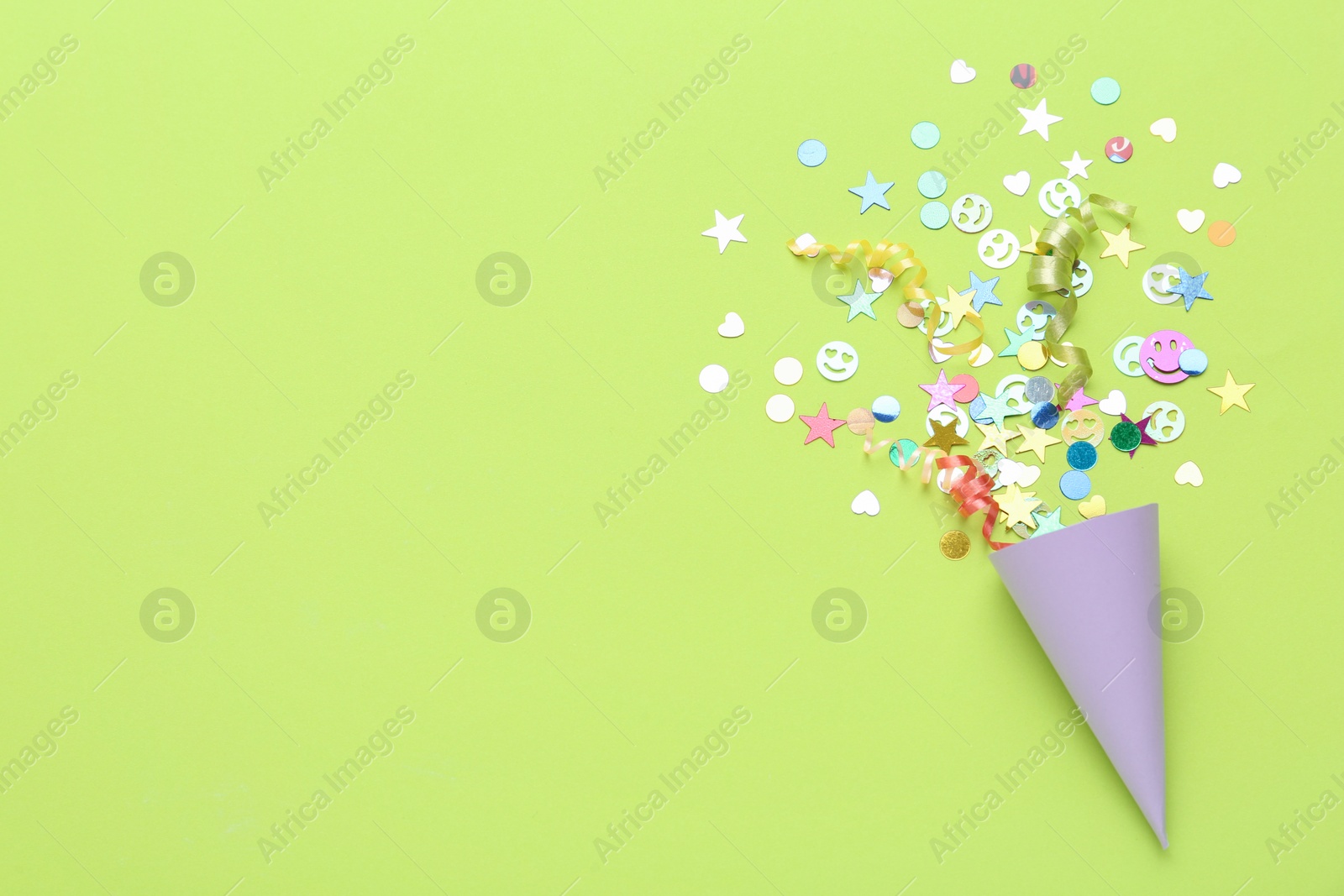 Photo of Colorful confetti and streamers with party cracker on light green background, top view. Space for text