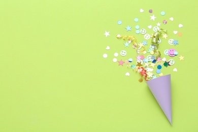 Colorful confetti and streamers with party cracker on light green background, top view. Space for text