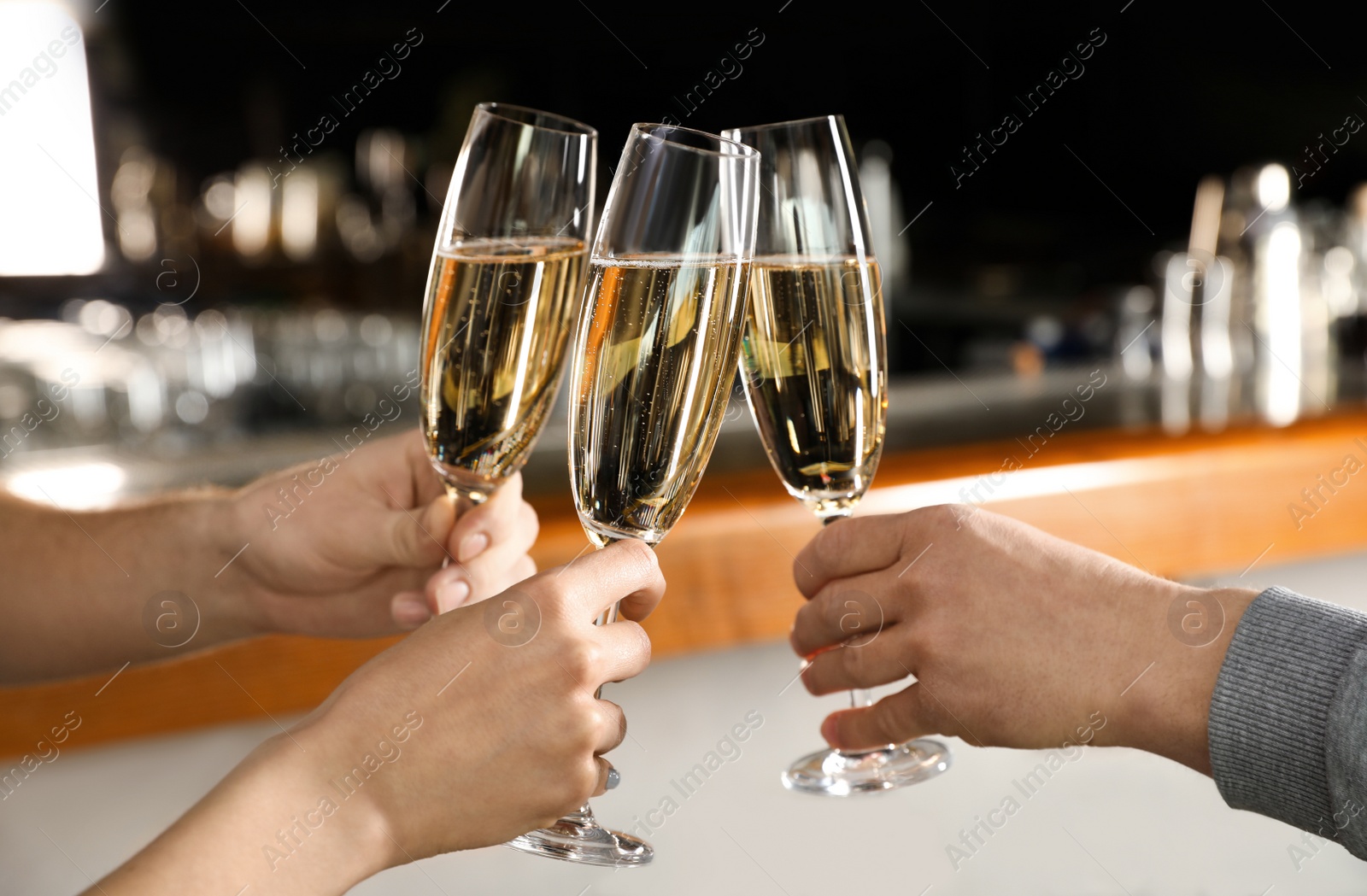 Photo of Friends clinking with glasses of champagne in bar, closeup