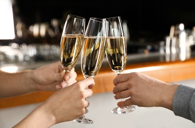 Photo of Friends clinking with glasses of champagne in bar, closeup