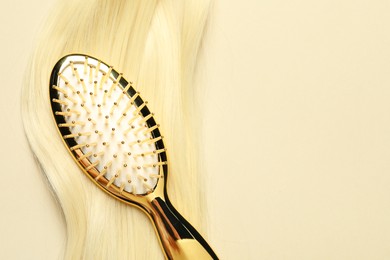 Photo of Stylish brush with blonde hair strand on beige background, top view. Space for text
