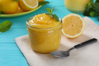 Photo of Delicious lemon curd in glass jar, fresh citrus fruits, mint and spoon on light blue wooden table