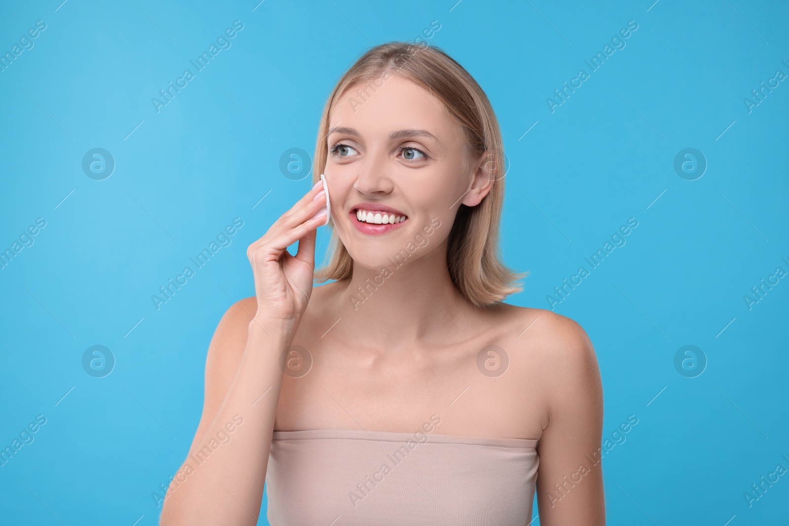 Photo of Young woman cleaning face with cotton pad on light blue background