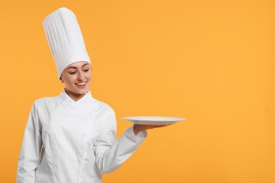 Photo of Happy professional confectioner in uniform holding empty plate on yellow background. Space for text