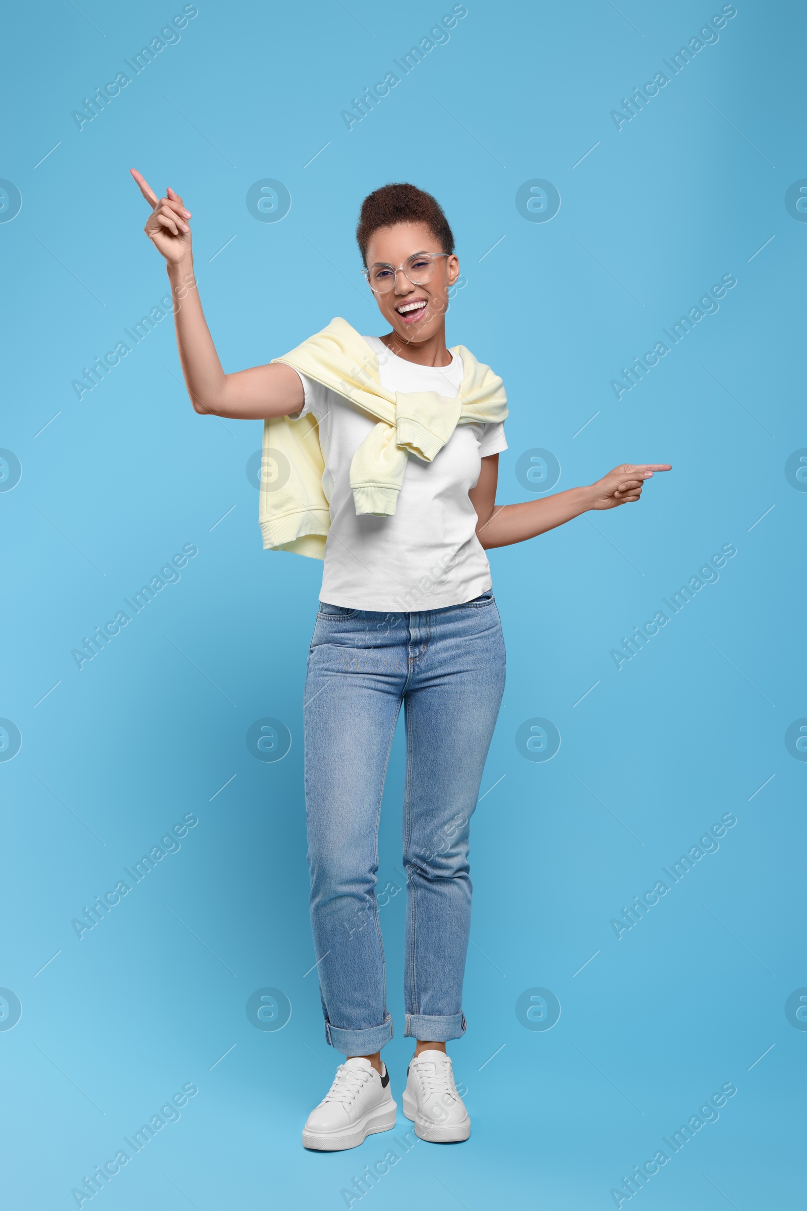 Photo of Happy young woman in stylish eyeglasses dancing on light blue background