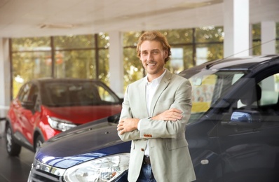 Young man near new car in modern auto dealership