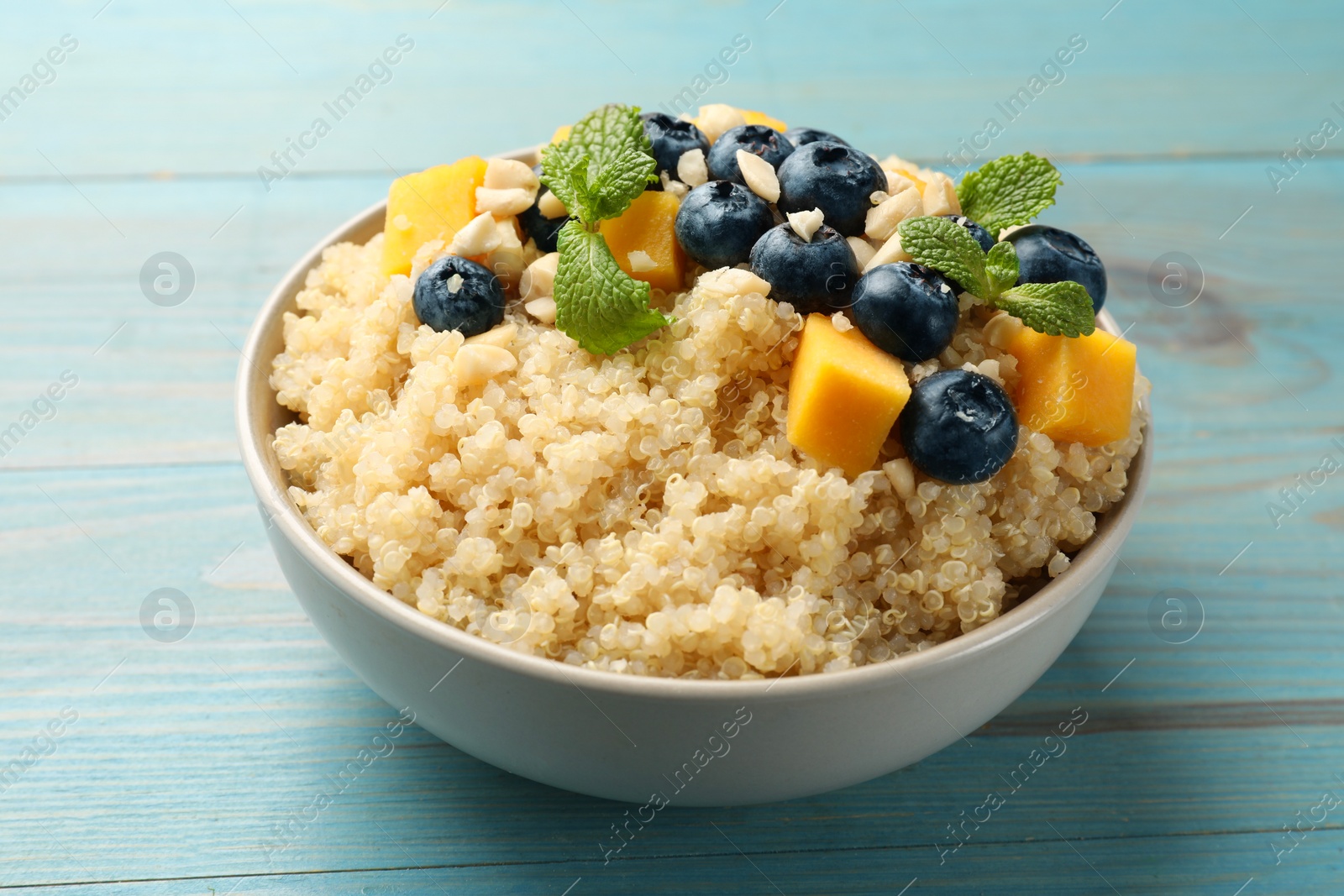 Photo of Tasty quinoa porridge with blueberries, pumpkin and mint in bowl on light blue wooden table, closeup