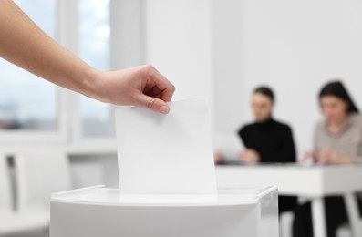 Photo of Woman putting her vote into ballot box on blurred background, closeup