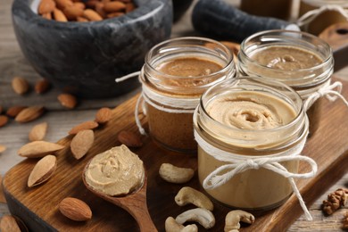 Photo of Tasty nut butters and raw nuts on wooden table, closeup