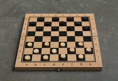 Photo of Wooden checkerboard with game pieces on grey table