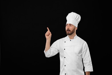 Photo of Mature chef pointing at something on black background, space for text