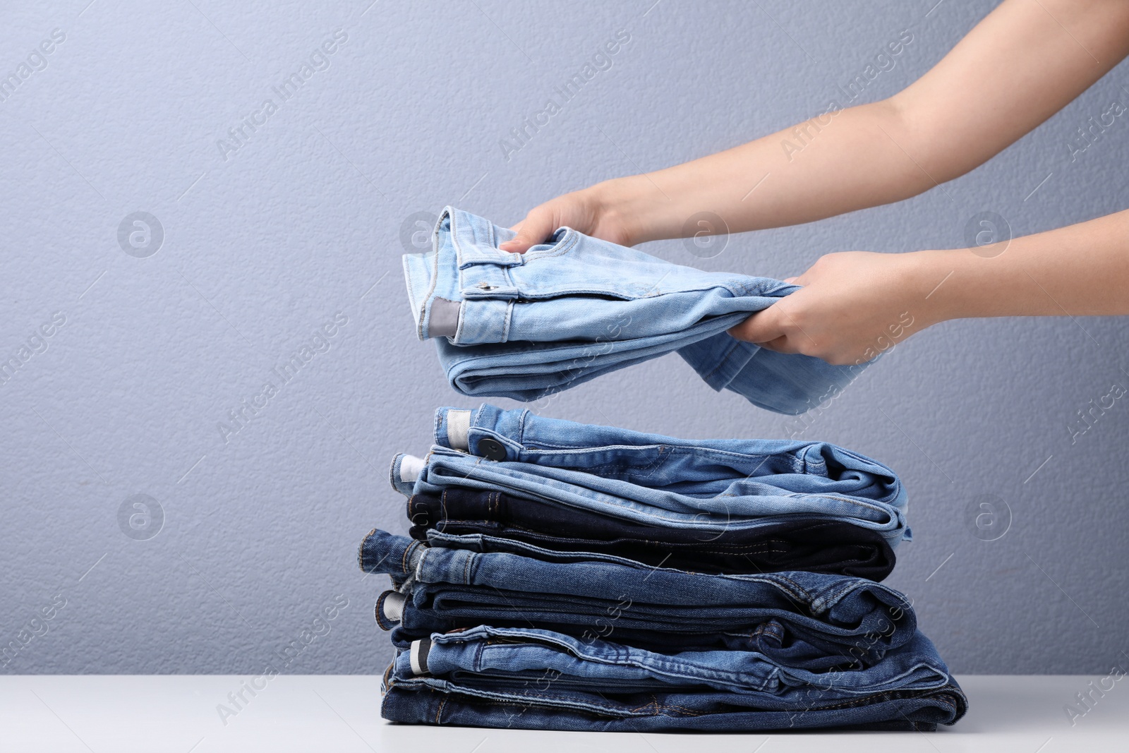 Photo of Young woman folding stylish jeans on table