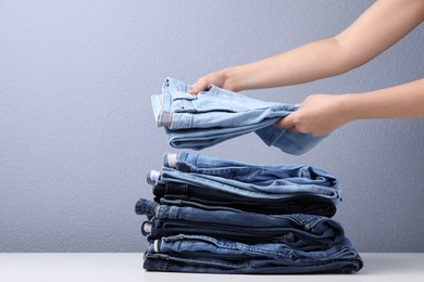 Photo of Young woman folding stylish jeans on table