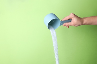 Photo of Woman pouring laundry detergent from measuring container against green background, closeup. Space for text