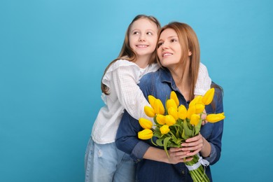 Photo of Mother and her cute daughter with bouquet of yellow tulips on light blue background. Space for text